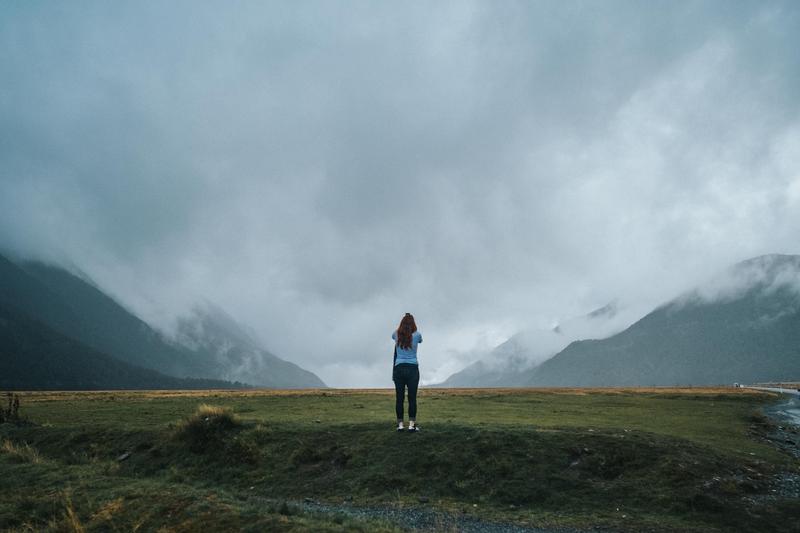 A woman stands below cloudy skies in the mountains