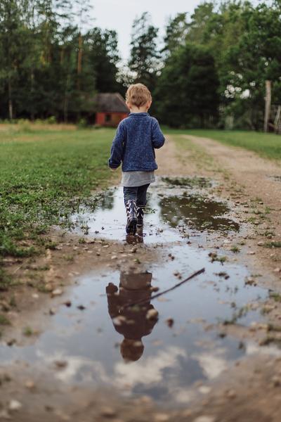 A young child trudges through a puddle on a country road