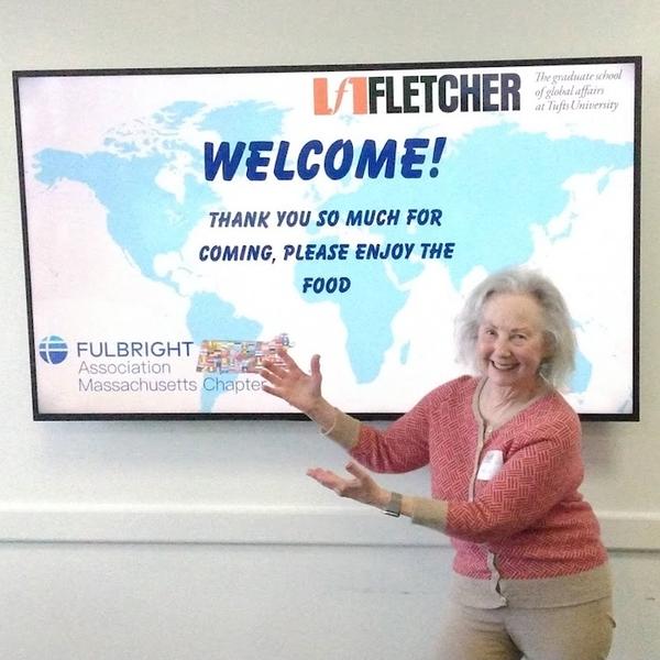Erlene smiling and gesturing toward a screen displaying a Fletcher School and Fulbright Association welcome message.