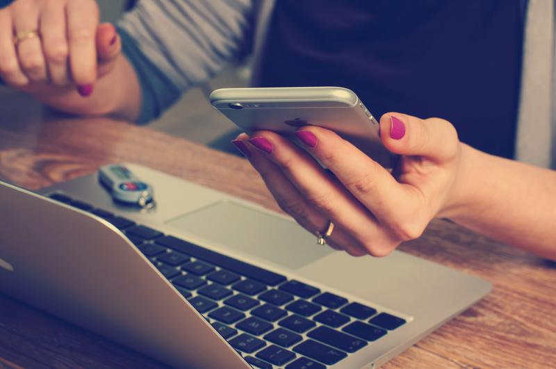 a senior's hands holding an iPhone while working at her computer