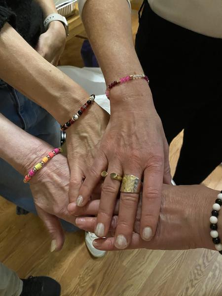 A group of people coming together in a gesture of unity by joining hands together, displaying various and distintive colorful bracelets and rings.